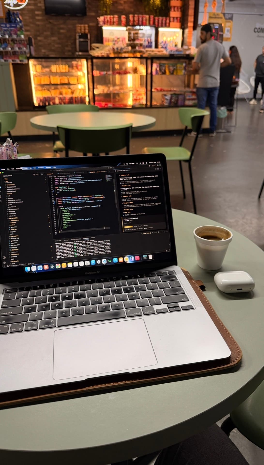 MacBook com código aberto ao lado de café e AirPods