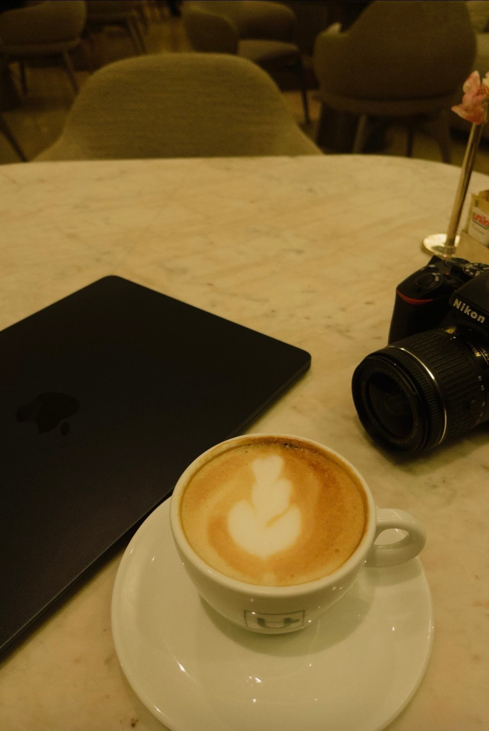 Coffee, a Nikon camera, and a closed MacBook on a café table
